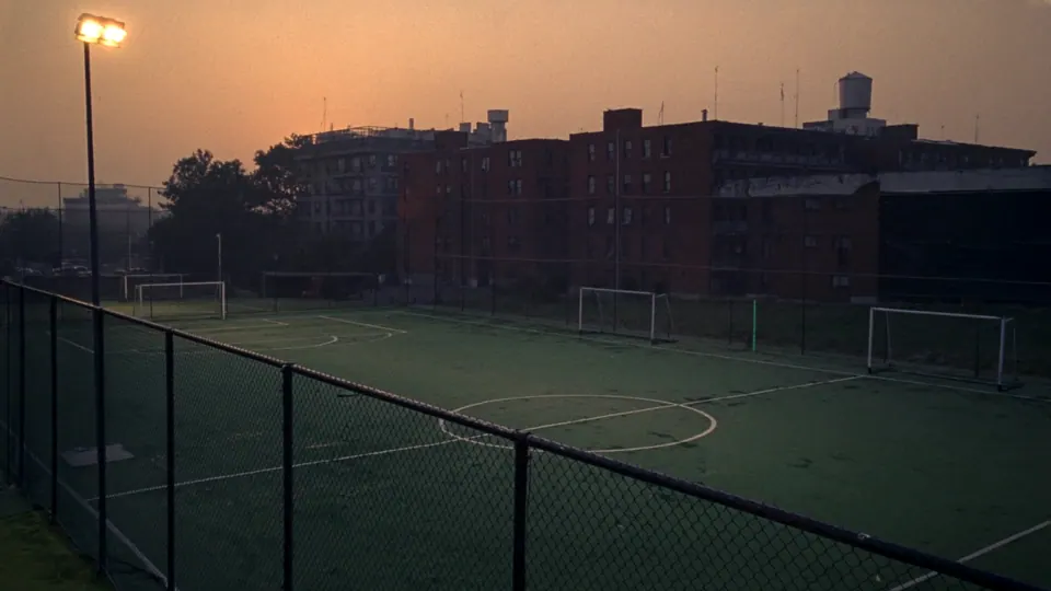 Schoolyard soccer pitch at dusk with brick apartment buildings behind
