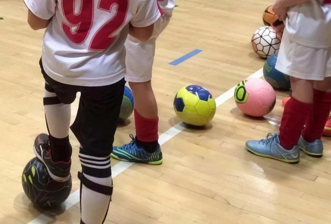 A training session: players in club kit with a ball each on the gym floor